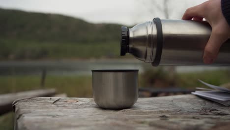 Eingießen-Von-Kaffee-Aus-Einer-Vakuumflasche-Aus-Stahl-Mit-Naturhintergrund