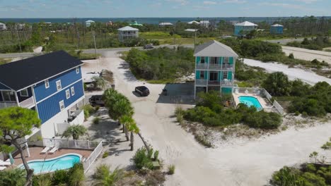 Drone-shot-of-vehicle-travelling-down-white-sandy-roads-passing-condos-at-Cape-San-Blas,-Florida