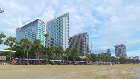 Playa-Frente-A-Tres-Hoteles-De-Gran-Altura-Con-Arena-Blanca-Y-Una-Gran-Variedad-De-Marquesinas-O-Sombrillas-Ocupadas-Por-Personas-Y-Niños.