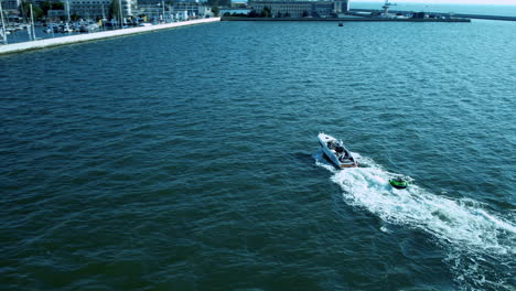 Aerial-view-of-a-boat-speeding-across-blue-water-near-a-coastal-city