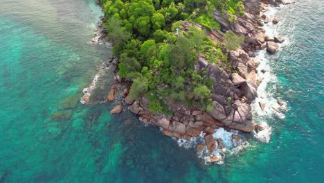 Drone-shot-of-hill-and-granites-rocks,-a-white-cross-and-turquoise-water-at-baie-Lazare-beach,-Mahe-Seychelles-30fps
