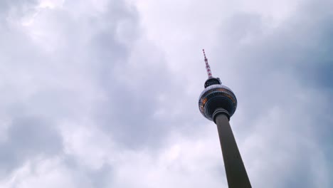 As-dawn-casts-a-subtle-light,-the-Fernsehturm-at-Alexanderplatz-reaches-skyward,-standing-firm-against-a-backdrop-of-grey-clouds-scurrying-across-the-awakening-sky