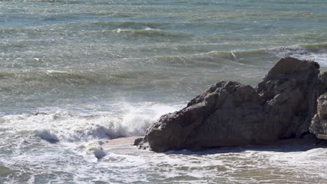 Rough-sea-with-waves-hitting-the-rocks-on-the-beach-at-midday