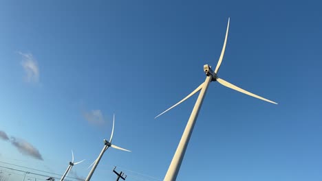 Under-blue-sunlight-sky-wind-turbines-rotate-in-unison,-handheld