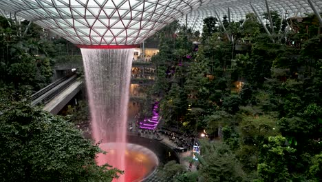 High-Angle-View-Overlooking-Red-Illuminated-The-Rain-Vortex-Indoor-Waterfall-At-Jewel-Changi-Airport-Singapore