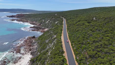 Aerial-drone-flying-over-cars-driving-along-winding-scenic-road-in-Margaret-River,-Western-Australia