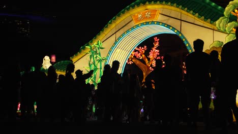 Silueta-De-Personas-En-Los-Jardines-Junto-A-La-Bahía-Festival-De-Mediados-De-Otoño-Exhibición-De-Linternas-Iluminadas-Por-La-Noche