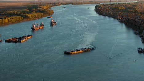 Aerial-shot-pusher-tug-pushing-barges-on-a-big-river,-illuminated-by-sunlight,-4K50Fps