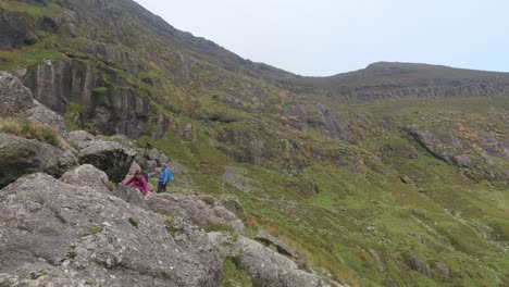 Las-Niñas-Escalando-Rocas-Con-Tomas-Panorámicas-Al-Lago-Coumshingaun-En-Lo-Alto-De-Las-Montañas-Comeragh-En-Waterford,-Irlanda,-En-Un-Perfecto-Día-De-Invierno