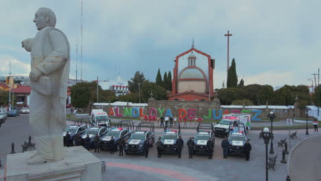Panorámica-Vertical-De-7-Camionetas-Policiales-Y-2-Ambulancias-Con-Agentes-Armados-Del-Departamento-De-Policía-Alineados-Y-Posando-Delante-De-Sus-Coches-Y-Detrás-De-Una-Estatua-Del-Presidente-Benito-Juárez.