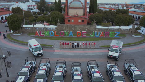 Forward-moving-shot-passing-by-7-police-pick-ups-and-2-ambulances-with-armed-officers-of-the-Police-Department-lined-up-and-posing-in-front-of-their-cars-and-behind-a-statue-of-President-Benito-Juarez