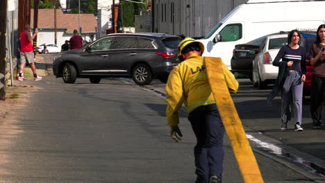 LAFD-Firefighter-draging-a-hose-on-the-streets-of-sunny-Los-Angeles,-USA