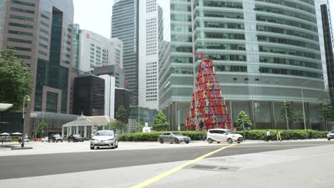 Traffic-Passing-Along-Marina-Blvd-And-Raffles-Quay-With-Momentum-Sculpture-In-Background,-Singapore