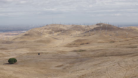Wide-shot-of-dry-hills-with-windmills-not-turning-in-background-on-cloudy-day