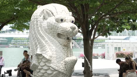 Mini-Escultura-Merlion-En-Singapur-Con-Turistas-Sentados-Bajo-Un-árbol-En-Segundo-Plano.