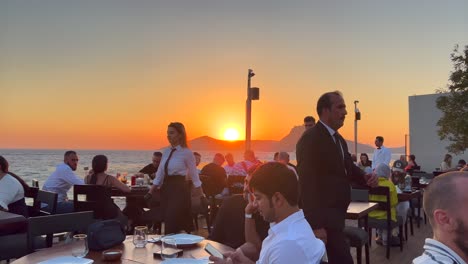 Beautiful-orange-sunset-at-Nusret-Salt-Bae-restaurant-in-Yalikavak-port,-luxury-dining-experience-at-a-famous-restaurant-in-Bodrum-Turkey,-4K-static-shot