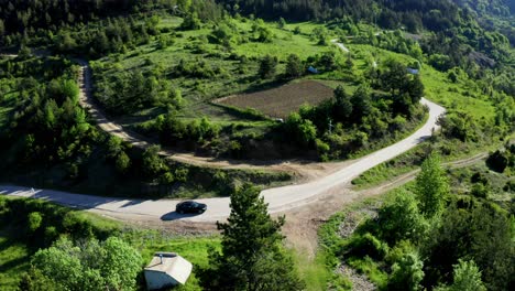 Black-Vehicle-on-hilly-road-in-green-Rhodope-Mountains-during-sunny-day,-Bulgaria