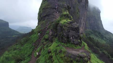 Disparo-De-Un-Dron-Que-Revela-El-Paisaje-Del-Antiguo-Fuerte-De-Harihar-Con-Turistas-Bajando-Escaleras-Empinadas-Y-Verticales-Durante-La-Caminata-Monzónica,-Hardewadi,-Trimbak