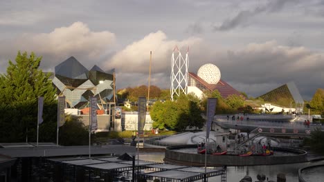 Panoramic-view-of-the-Futuroscope-theme-park-with-peo9ple-walking-on-platforms-on-a-windy-day,-Wide-shot