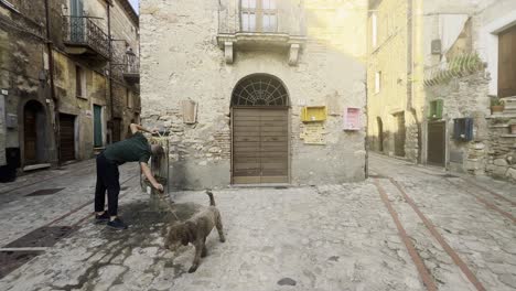 Man-and-dog-drinking-at-street-fountain-during-grape-harvest-festival-of-medieval-Penna-in-Teverina-town-with-decorated-houses-and-streets,-Italy