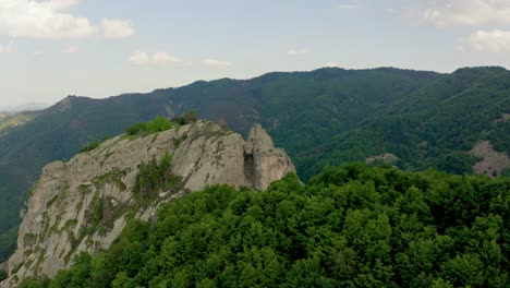 Aerial-approaching-shot-of-famous-The-Karadzhov-Boulder-in-Rhodope-Mountains-during-sunny-day---Tourist-standing-on-edge