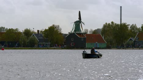 Men-On-Boat-Fishing-In-The-River-With-Windmill-In-The-Distance-In-Amsterdam