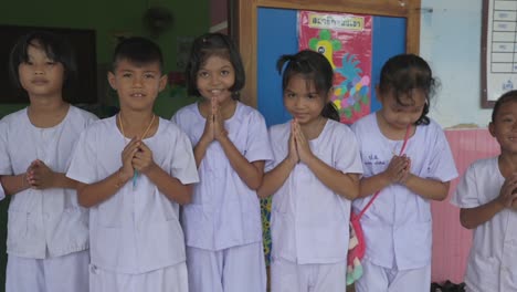 Los-Niños-Tailandeses,-Reunidos-Frente-A-Su-Salón-De-Clases,-Saludan-Calurosamente-A-La-Cámara-Con-Sonrisas-Brillantes,-Encarnando-El-Encanto-De-La-Juventud-Tailandesa-Y-El-Espíritu-De-Intercambio-Cultural.