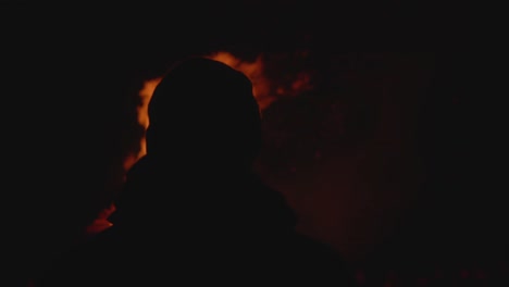 Silhouette-of-man-with-cap-watching-flames-of-a-fire-at-night