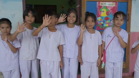 Thailändische-Schüler,-Die-Vor-Ihrem-Klassenzimmer-Stehen,-Winken-Begeistert-In-Die-Kamera-Und-Strahlen-Dabei-Wärme-Und-Freude-Am-Lernen-Aus