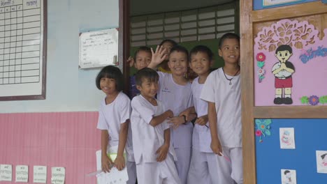 In-the-doorway,-Thai-kids-wave-goodbye,-their-smiles-radiating-warmth-as-they-bid-farewell,-creating-a-touching-moment-of-shared-connection
