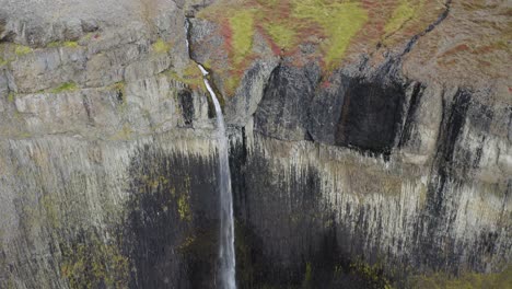 Aerial-backwards-shot-waterfall-falling-in-volcanic-scenery-of-Iceland-during-daytime