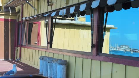 Light-breeze-moving-awning-and-reflection-on-the-window-of-water-and-boats-with-seagull-in-Monterey's-Fisherman's-Wharf-restaurant