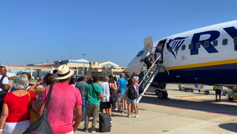 People-waiting-in-line-and-boarding-a-big-Ryanair-boeing-airplane-in-Malaga-international-airport-on-a-sunny-day-in-Spain,-holiday-vacation-time,-4K-static-shot