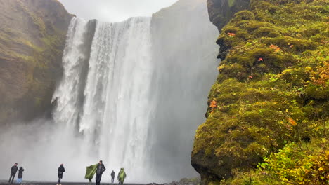 Personas-Con-Impermeables-Visitando-La-Increíble-Cascada-De-Skogafoss-En-Islandia