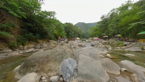 Aerial-flight-over-Rio-Bani-River-with-people-resting-on-shoreline,-Dominican-Republic