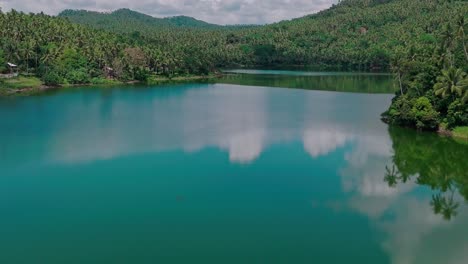 An-aerial-drone-shot-of-Mahucdam-Lake,-Surigao-Del-Norte,-Philippines,-showing-beautiful-still-reflections-of-the-surrounding-lush-jungle