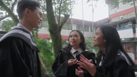 Group-of-Friend-Wearing-Graduation-Gown-Joking,-Talking,-Chatting-Happily-During-Rainy-Cloudy-Day