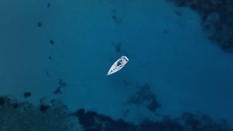 Drone-top-down-static-of-sailboat-anchored-in-stunning-clear-blue-ocean-water