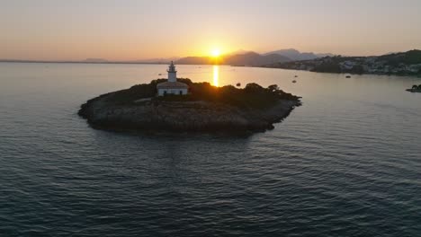 Sun-sets-behind-mountains-casting-golden-light-across-ocean-leading-to-Alcanada-lighthouse