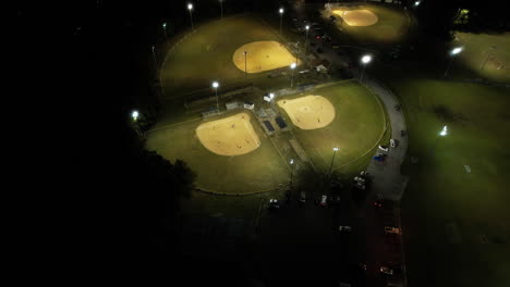 Aerial-shot-of-baseball-fields-at-night,-wide-drone