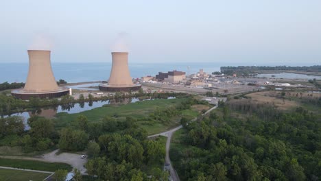 Nuclear-power-plant-chimneys-with-rising-smokes-on-lake-coastline,-aerial-view