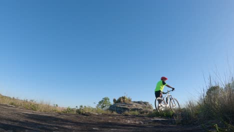 Cyclist-pushing-his-bike-on-a-trail,-blue-sky-in-the-background