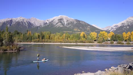 Paddle-boarder-with-dog-on-the-Bow-river-in-Canmore,-AB-wide-side-shot