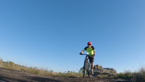 Cyclist-pedaling-on-a-natural-trail-with-a-blue-sky-in-the-background