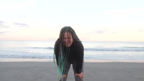 woman-with-braids-smiles-tired-after-running-at-beach