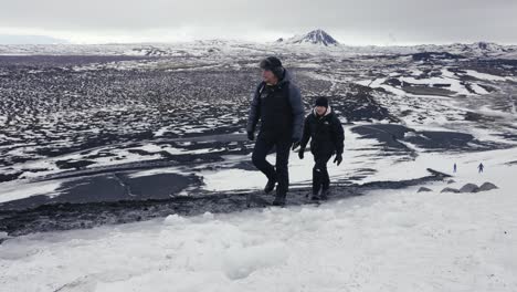 Father-and-son-climb-Hverfjall-Volcano,-black-rock-landscape-in-background