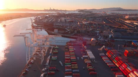 Cranes-in-a-large-container-port-at-sunset,-aerial-establishing-view