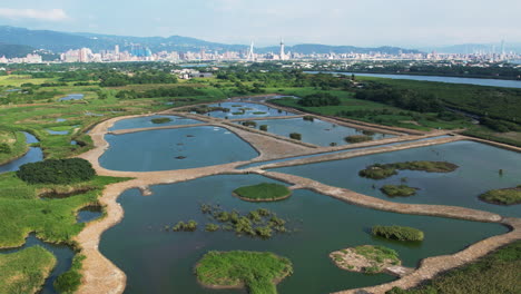 Panoramic-aerial-overview-of-wetlands-at-Guandu-nature-park,-Taipei-skyline-behind