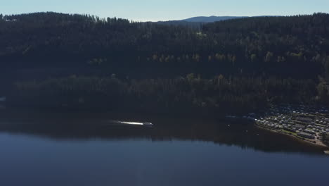 Approaching-shot-of-a-tourist-boat-far-away-on-a-lake-in-the-Black-Forest-with-a-campsite-on-the-right-at-summer