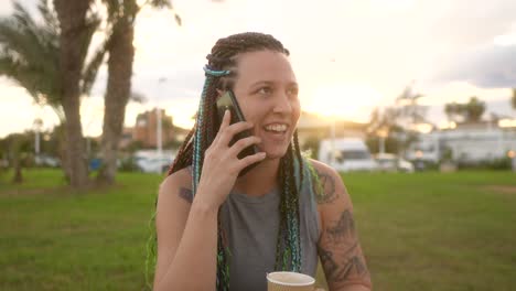 Mujer-Con-Trenzas-Y-Sonrisa-Hablando-Por-Teléfono-Inteligente-En-El-Parque